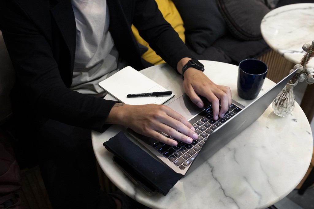 Hands on a laptop keyboard, notebook beside